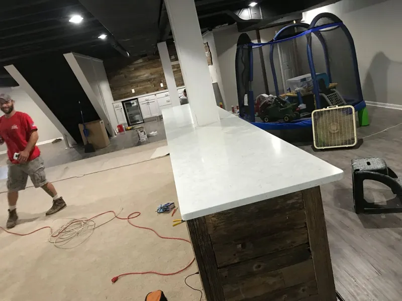 Stone Proz installer setting a white countertop in a basement bar